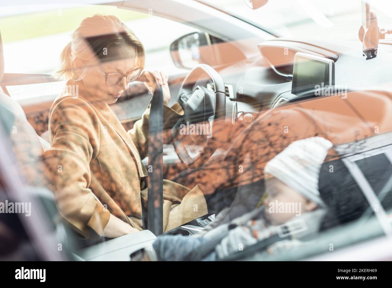 Mutter befestigt den Sicherheitsgurt, fährt mit einem Familienauto und führt Besorgungen durch, während ihr Baby auf dem Kinderautositz neben ihrem Standort schläft Stockfoto