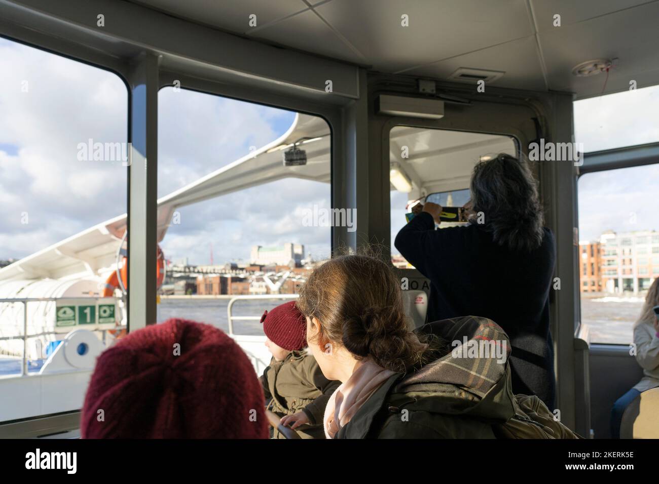 Touristen, die aus den Fenstern eines City Cruises Thames-Bootes auf die Sehenswürdigkeiten und Wahrzeichen Londons blicken, hier die Millenium Bridge - London, Großbritannien Stockfoto