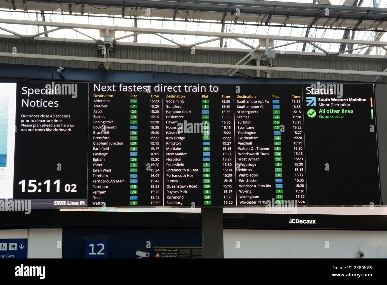 Live-Abflugtafel mit den schnellsten Zügen zu verschiedenen Zielen und Zug am Bahnhof Waterloo. London, England Stockfoto