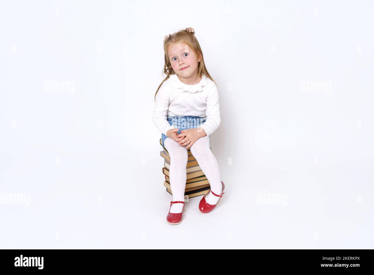 Porträt eines kleinen Mädchens, das auf Büchern sitzt. Isoliert auf weißem Hintergrund. Stockfoto