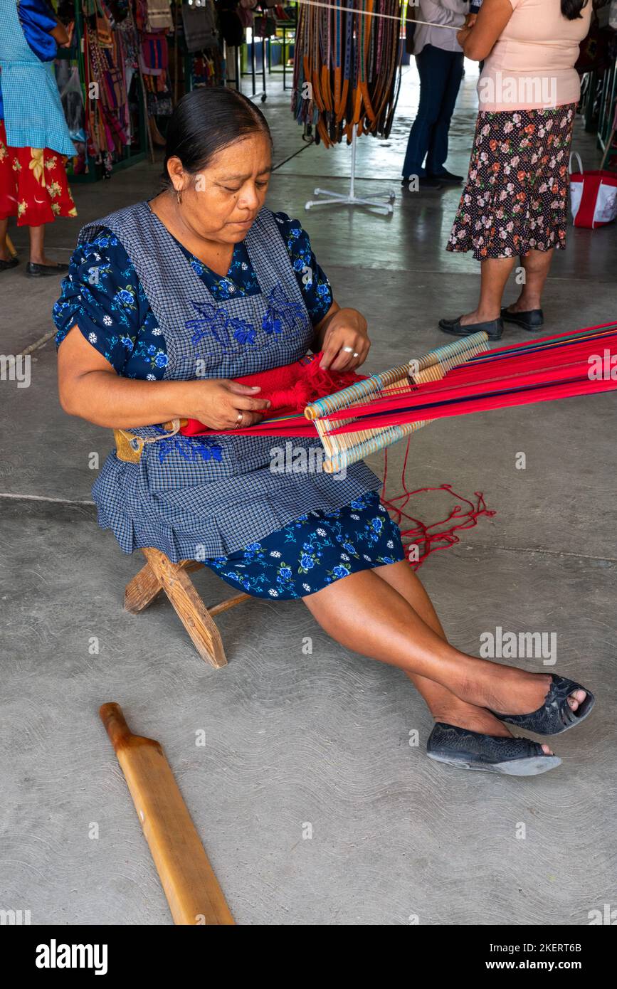 Eine Frau, die eine traditionelle Schürze trägt, webt Stoff auf einem traditionellen Webstuhl mit Rückenband in Santo Tomas Jalieza, Mexiko. Jalieza ist berühmt für seine Webweine. Stockfoto