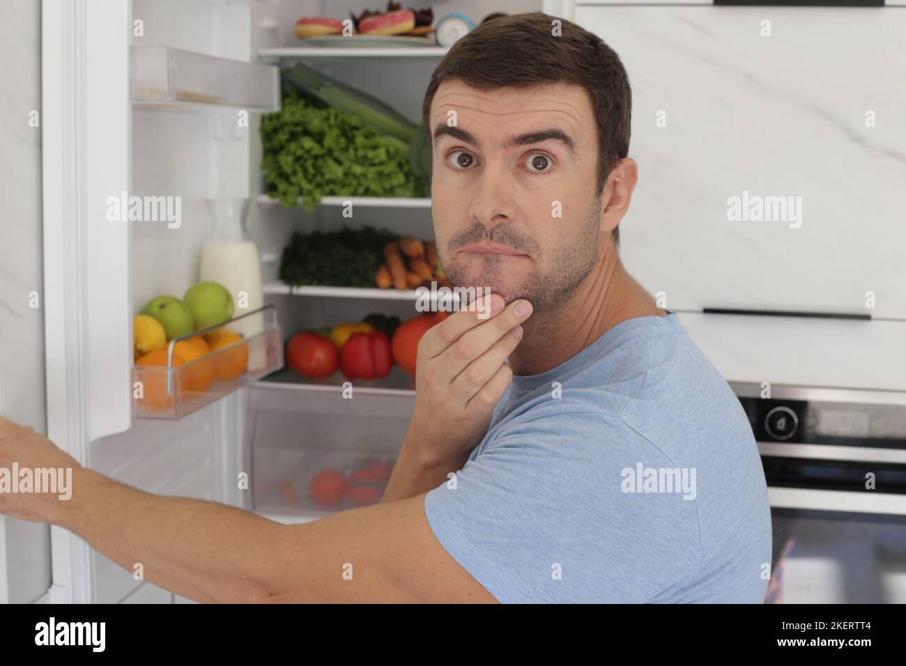Ein Mann öffnet die Kühlschranktür mit Zweifeln Stockfoto