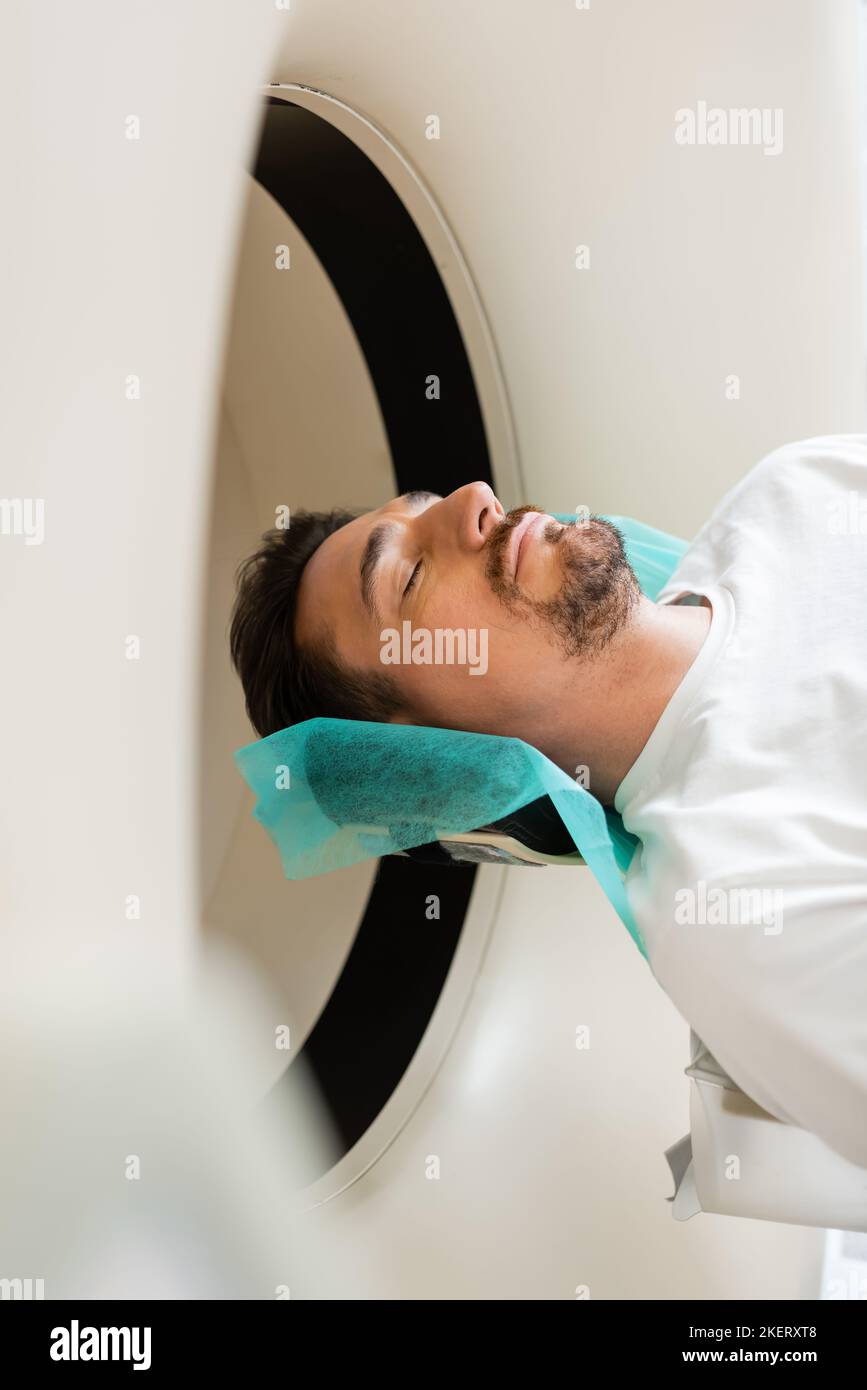 Bärtiger Mann mit geschlossenen Augen, der während der Diagnose auf der Computertomographie-Maschine lag, Stockbild Stockfoto