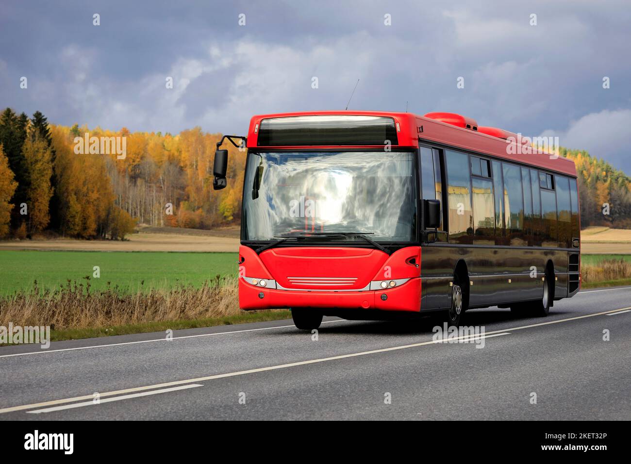 Bus mit roter Front, der an einem bewölkten Herbsttag auf der Autobahn durch die ländliche Landschaft fährt. Stockfoto