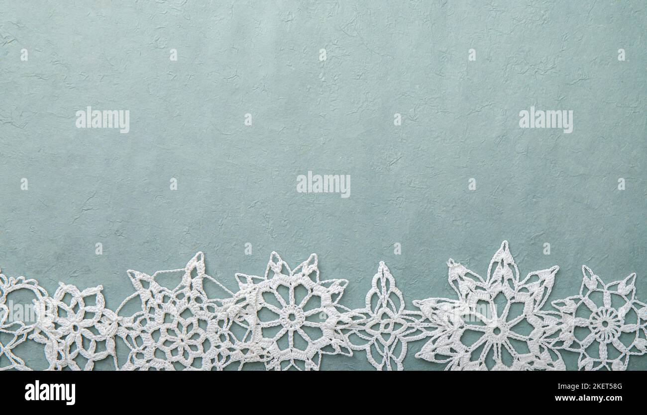 Hintergrund für Weihnachten- oder Winterprodukte, blaues grobes Bastelpapier mit handgefertigten Häkelschneeflocken, viel Platz für Kopien. Stockfoto