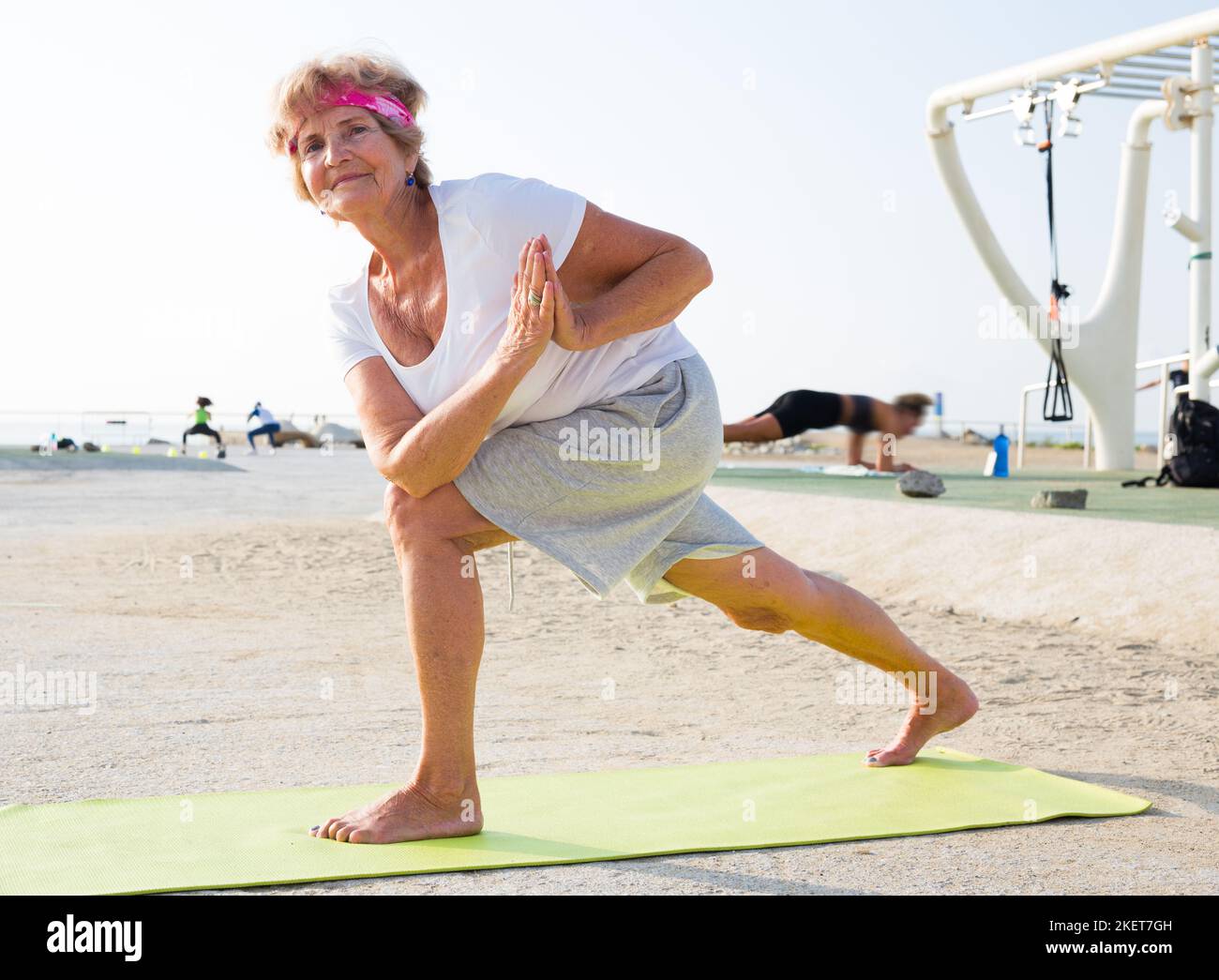 Alte Frau steht in Yoga-Pose im Freien Stockfoto