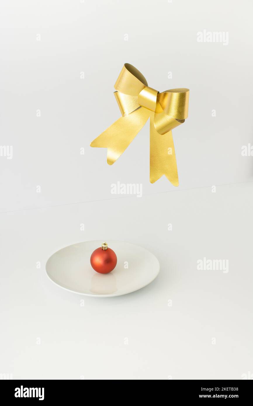 Rote Weihnachtskugel Dekoration auf weißem Teller mit goldener Schleife schweben oben. Minimales Neujahrskonzept. Stockfoto
