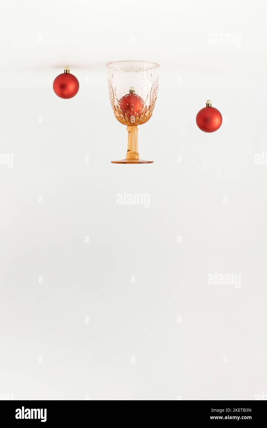 Vintage-Trinkglas und rote Weihnachtskugeln auf weißem Hintergrund umgedreht. Minimales Neujahrskonzept. Stockfoto