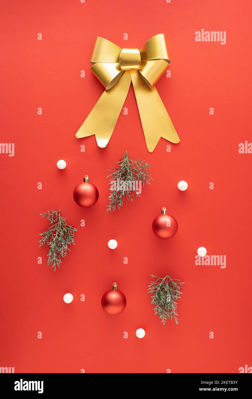 Goldene Schleife, rote Weihnachtskugeln, immergrüne Äste und weiße Kugeln auf rotem Hintergrund. Minimales Neujahrskonzept. Stockfoto