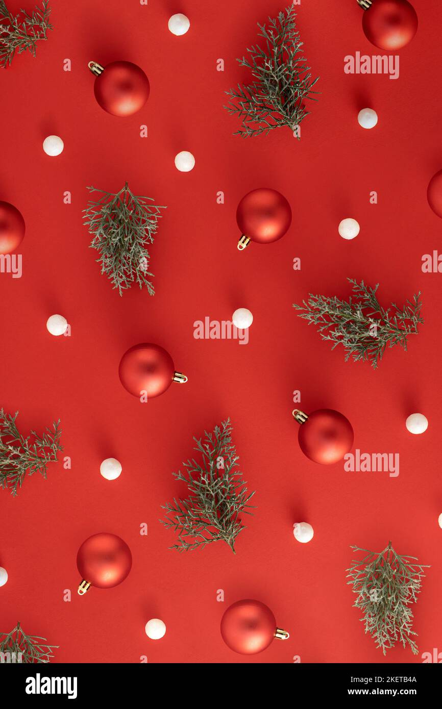 Weihnachtsmuster mit roten Kugeln, immergrünen Ästen und weißen Kugeln auf rotem Hintergrund. Minimales Neujahrskonzept. Stockfoto