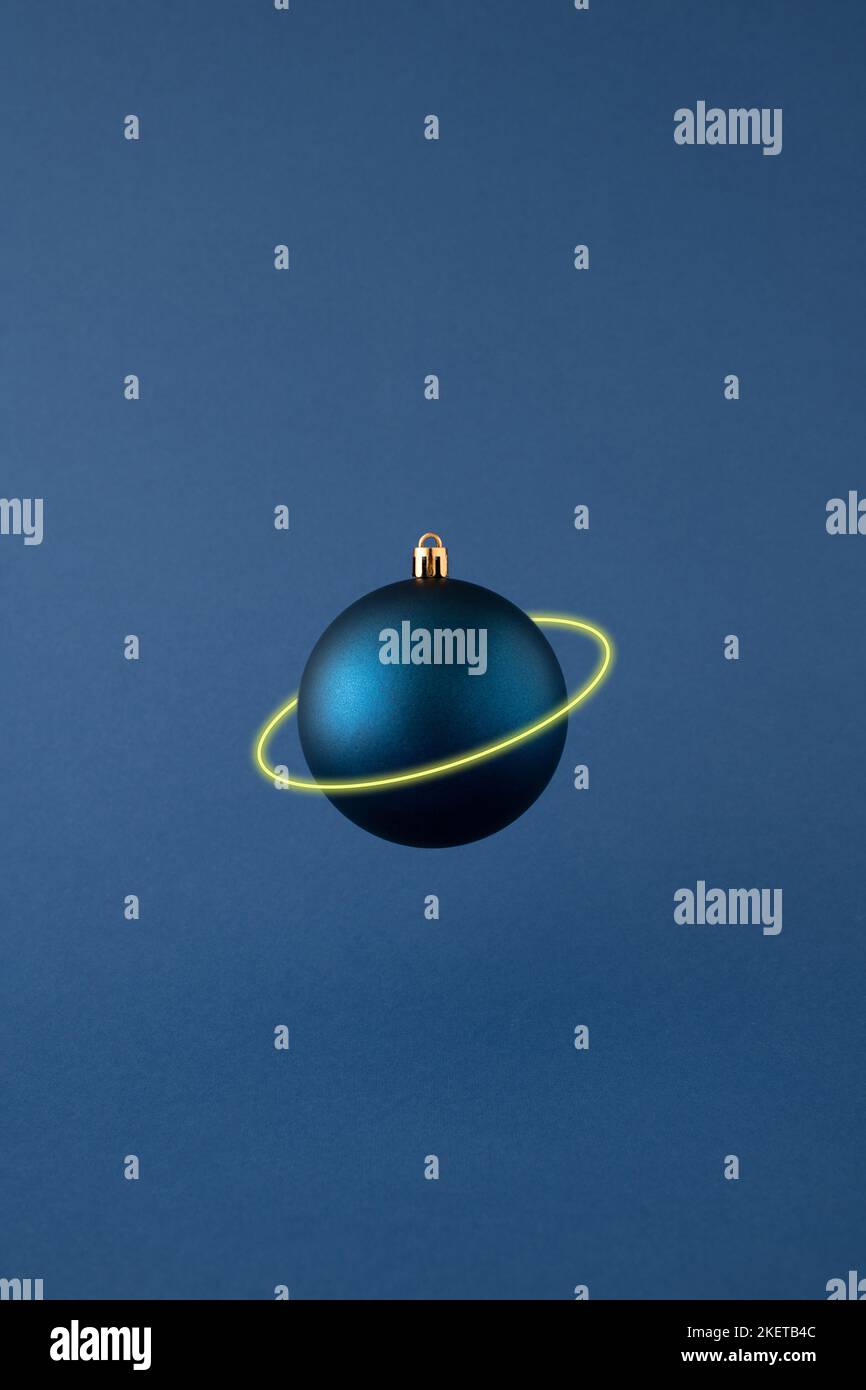 Blaue Weihnachtskugel schweben isoliert mit Neon Saturn Ring auf blauem Hintergrund. Minimales Neujahrskonzept. Stockfoto
