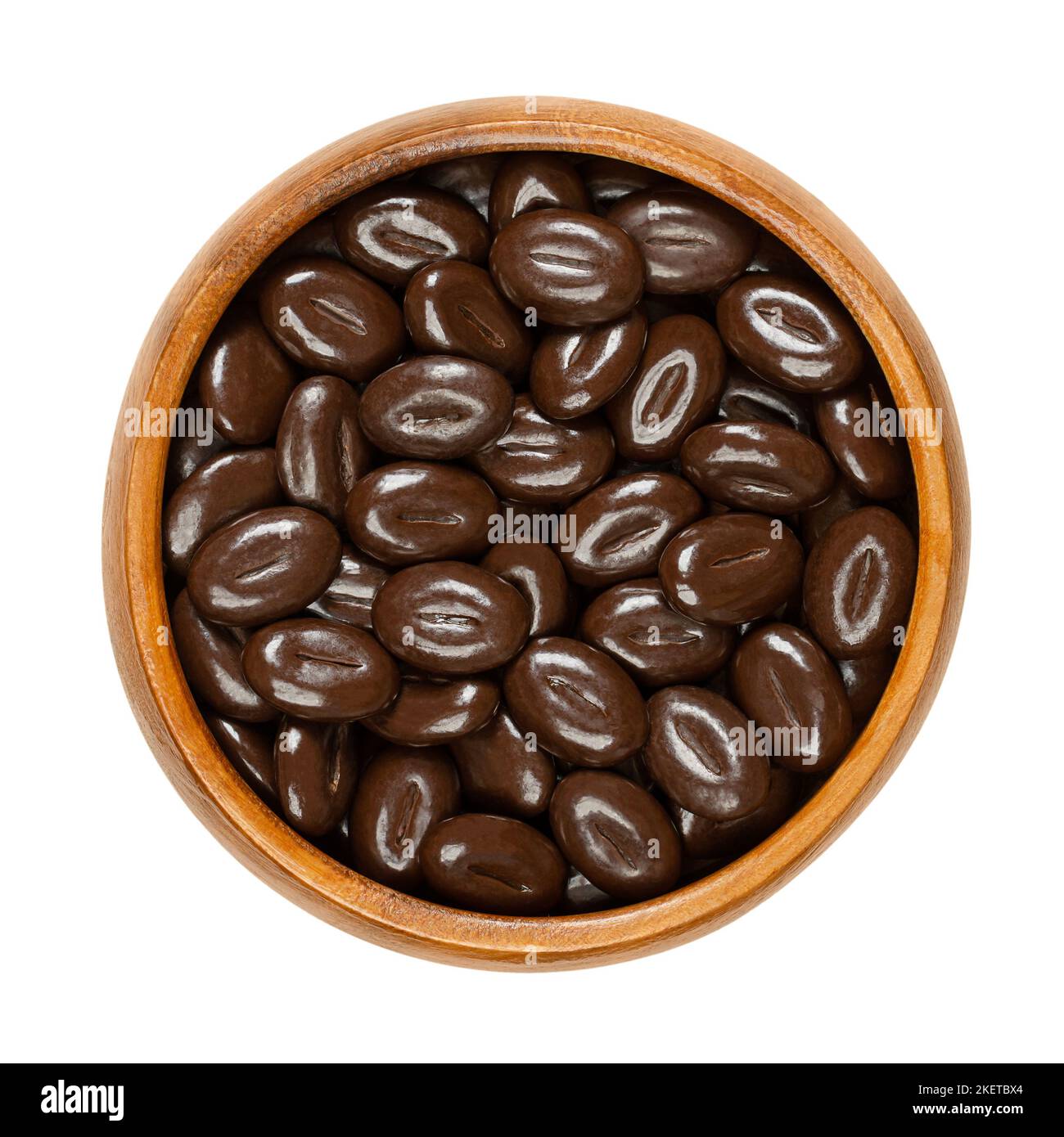 Mokka-Bohnen aus dunkler Schokolade, in einer Holzschüssel. Bonbons aus einer Mischung aus Kaffeebohnen-Geschmack mit dunkler Schokolade, in Form von Kaffeebohnen. Stockfoto