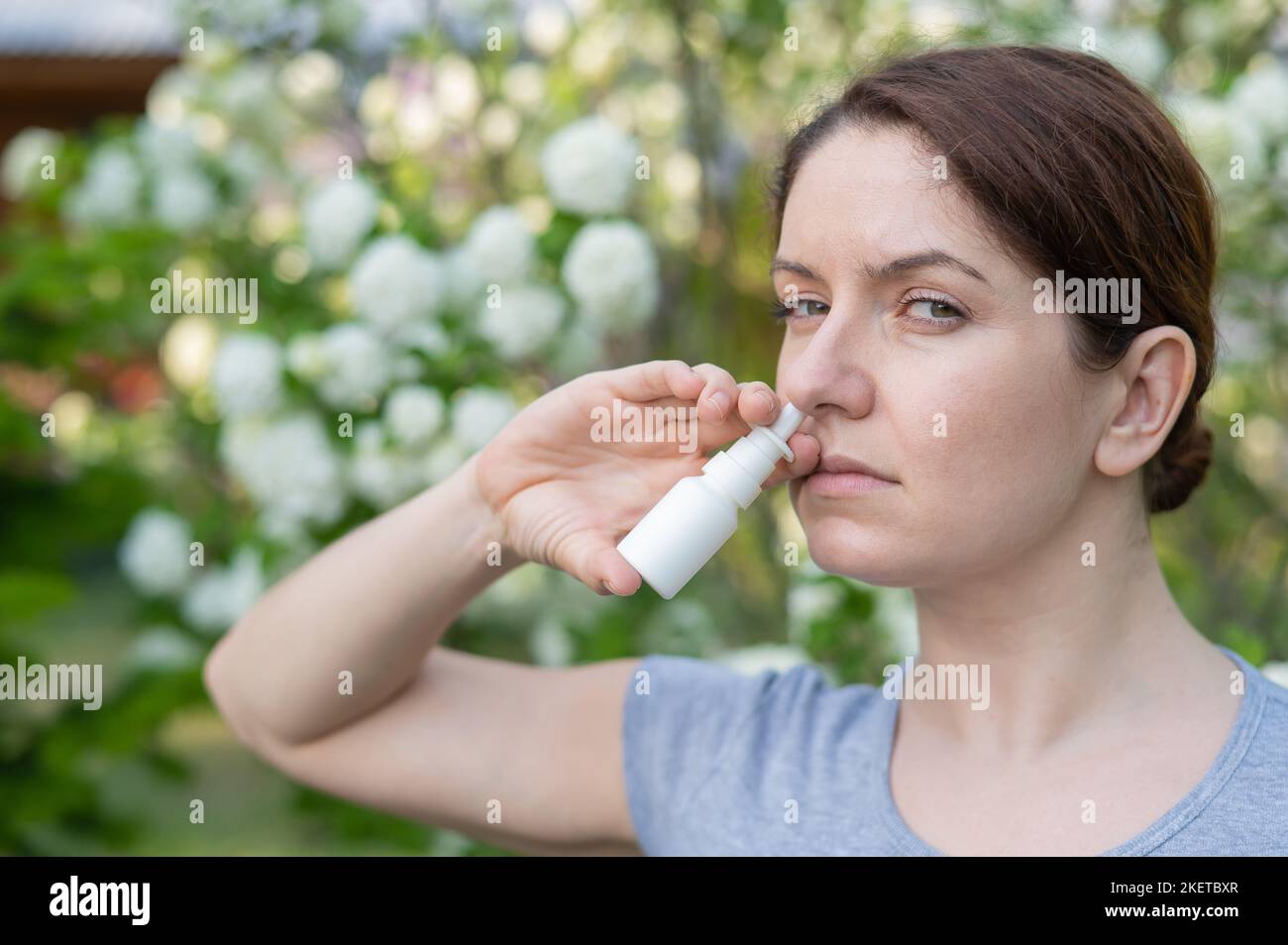 Kaukasische Frau verwendet ein Nasenspray, während sie im Park spazieren geht. Stockfoto