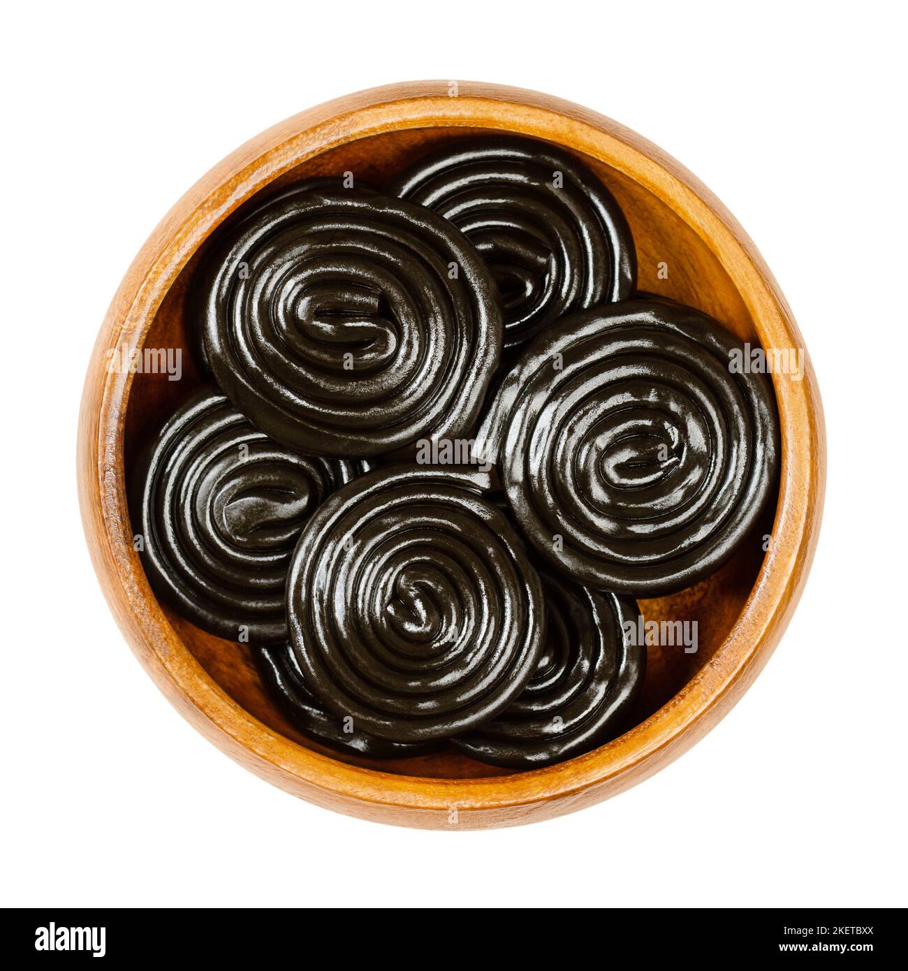 Lakritzräder, in einer Holzschale. Lakritze, ist eine Konfektion, in der Regel aromatisiert und schwarz gefärbt mit dem Extrakt der Wurzeln der Lakritzpflanze. Stockfoto