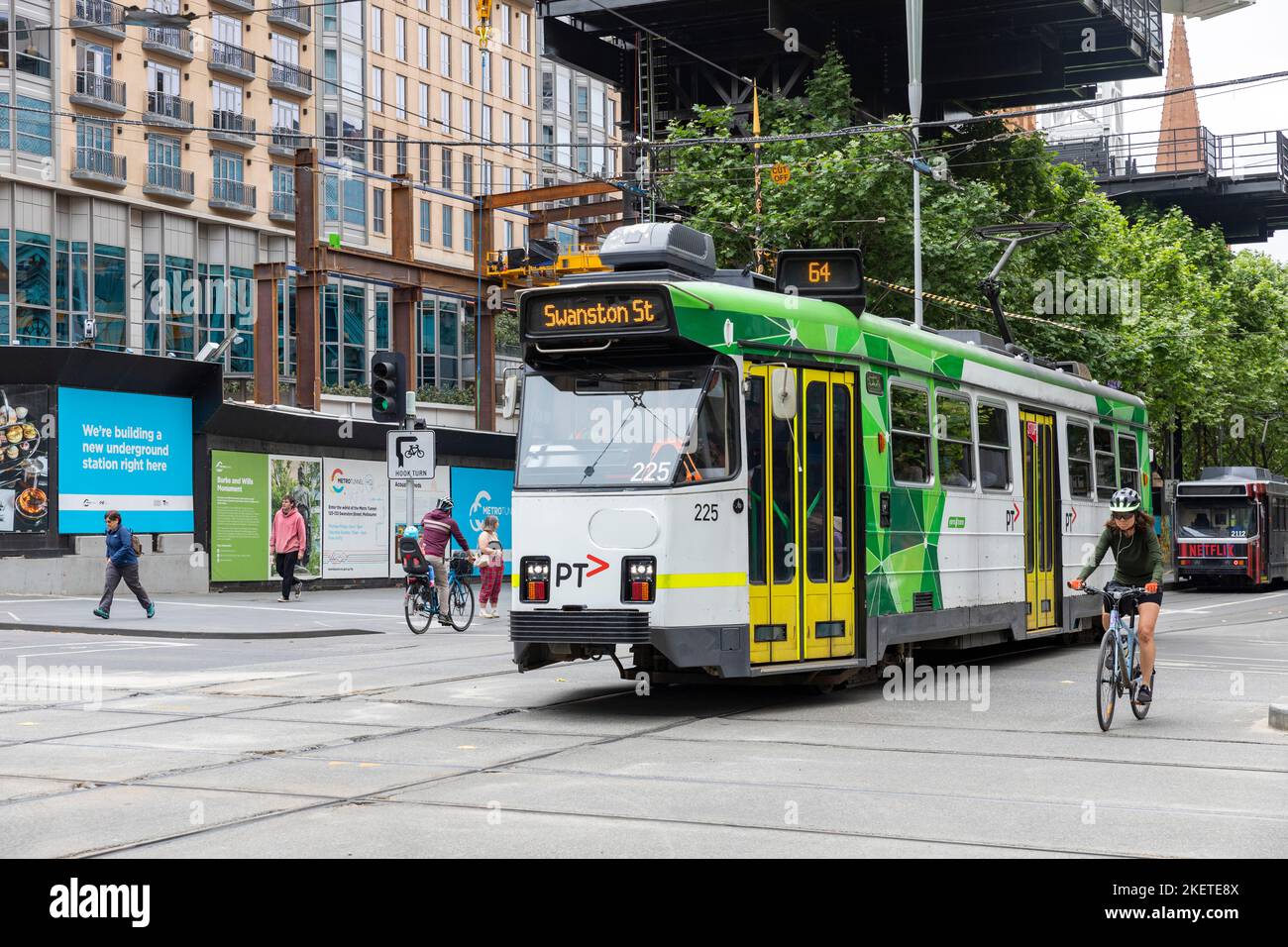 Frau, die an einem Frühlingstag im Jahr 2022 mit dem Fahrrad neben einer Straßenbahn im Stadtzentrum von Melbourne, Victoria, Australien, unterwegs ist Stockfoto