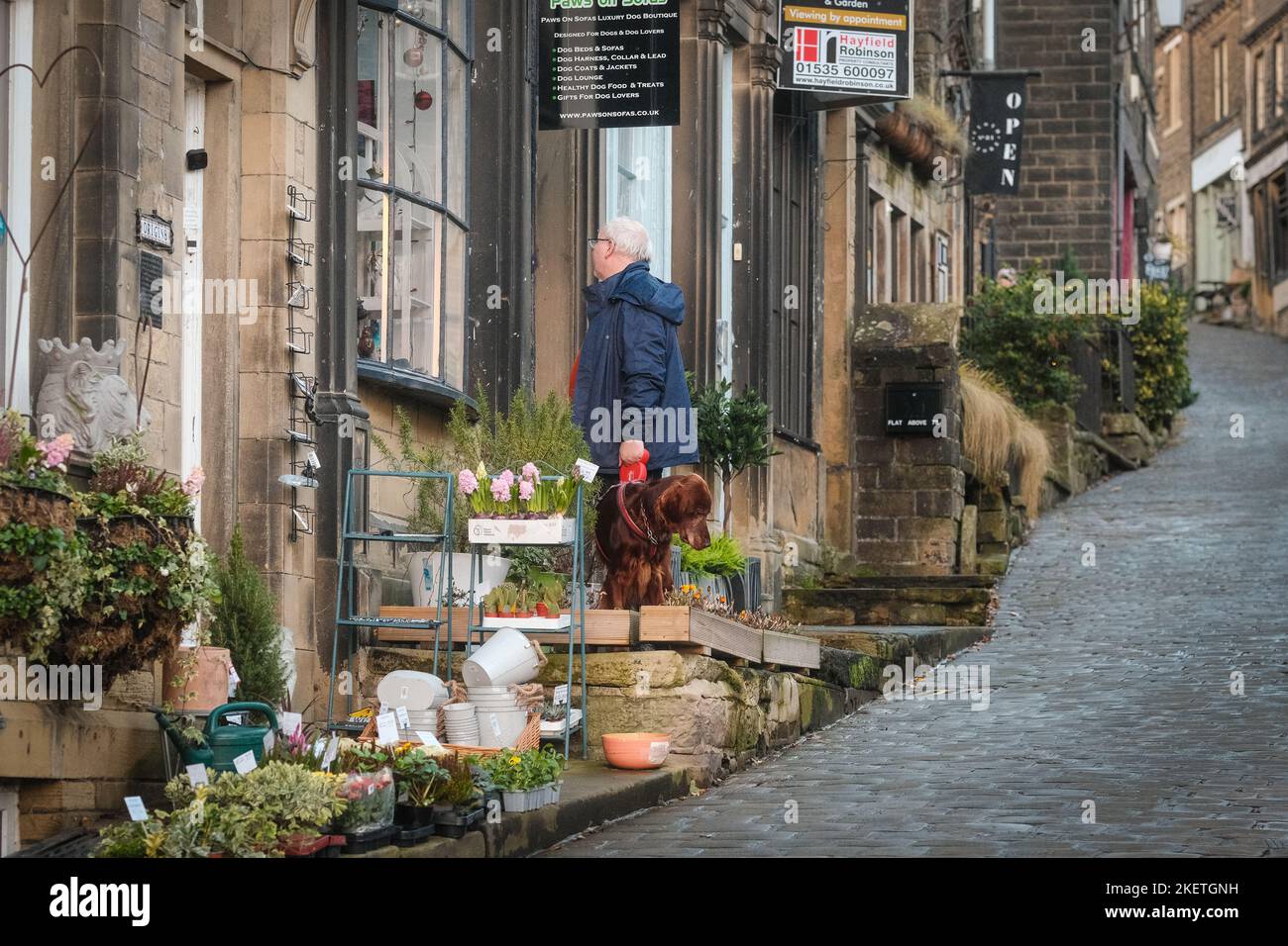 Haworth, West Yorkshire, Großbritannien. Ein Mann, der draußen stand und in einem Geschäft auf der Main Street schaute, Haworth mit seinem Hund. Stockfoto