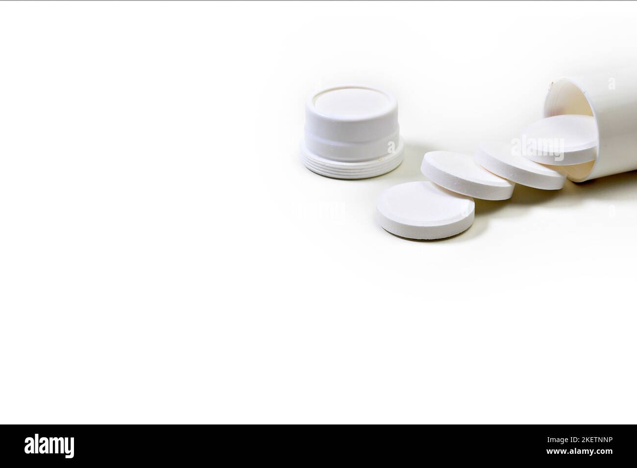 Weiße Medikamentenpillen verschüttet aus einer weißen Flasche auf weißem Hintergrund. Stockfoto