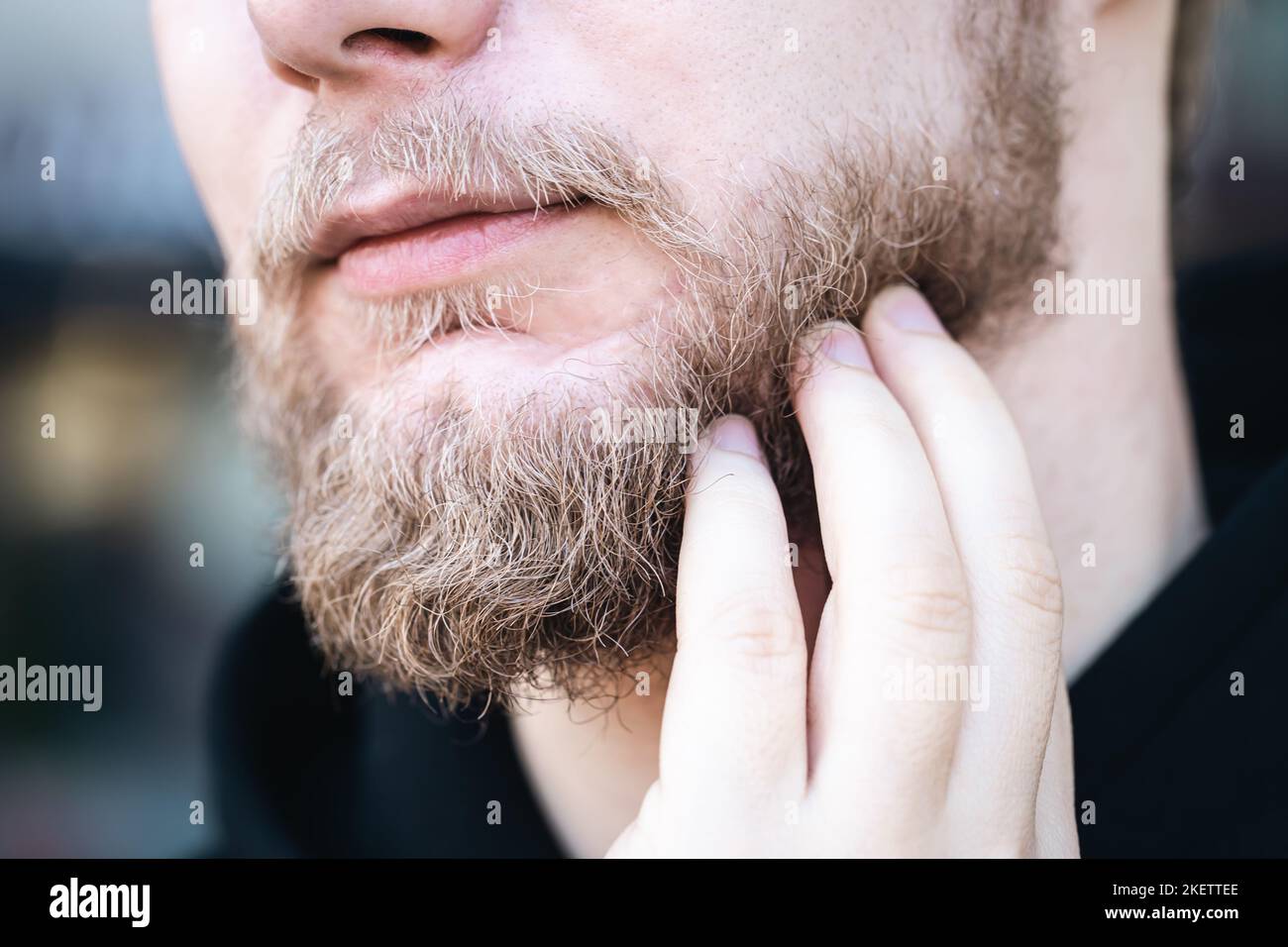 In Nahaufnahme berührt ein junger Mann seinen Bart mit der Hand. Stockfoto