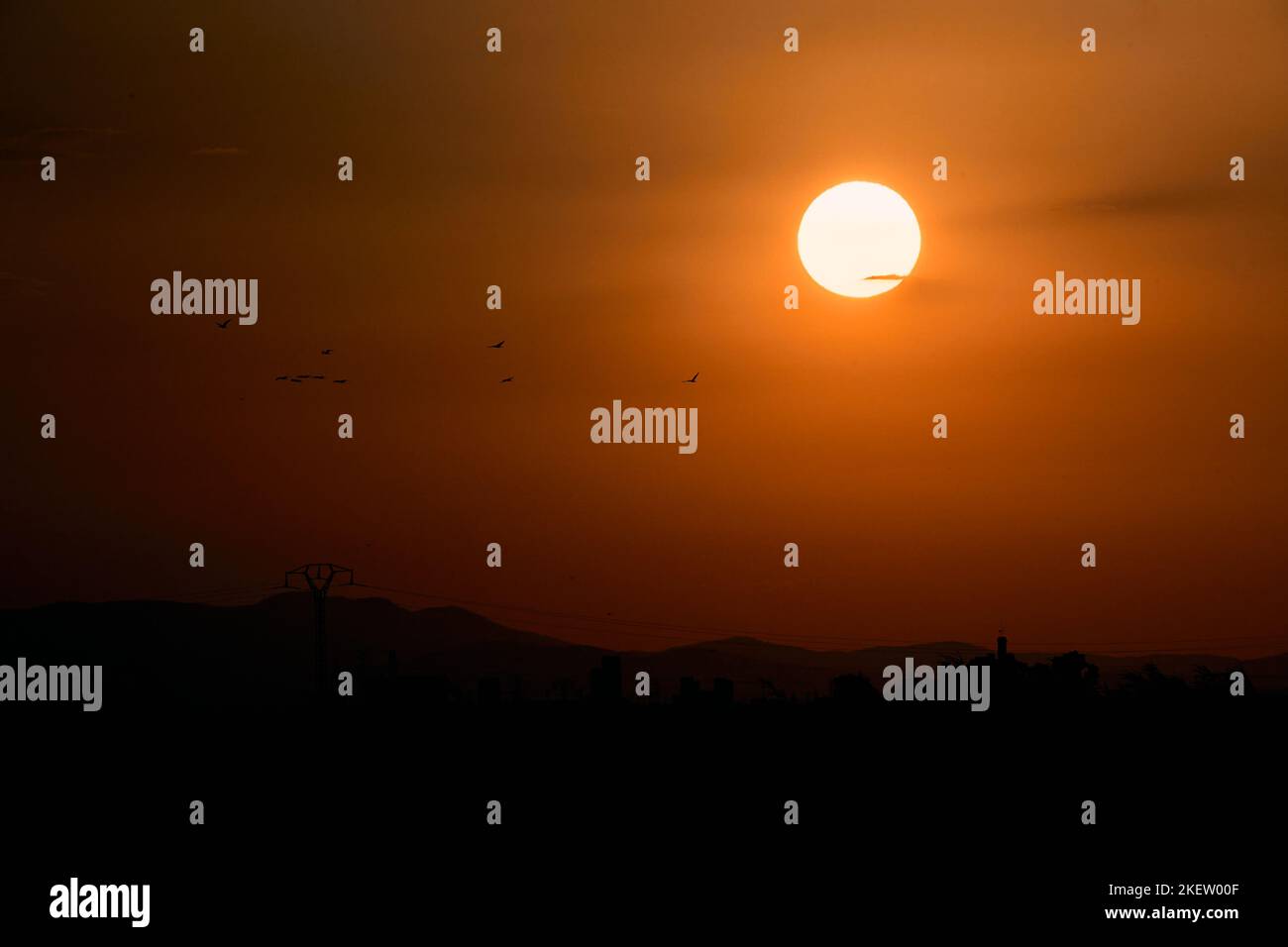 Runde gelbe Sonne in einem orangefarbenen Himmel bei Sonnenuntergang mit einigen Vögeln in der Nähe Stockfoto