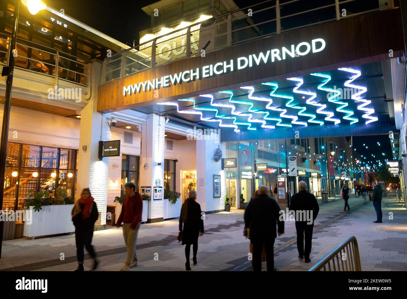 Cardiff Bay Walisisches Sprachschild 'wynhewch eich diwrnod' (Genießen Sie Ihren Tag) Einkaufsviertel Fußgängerzone bei Nacht zu Fuß Cardiff Wales UK 2022 Stockfoto