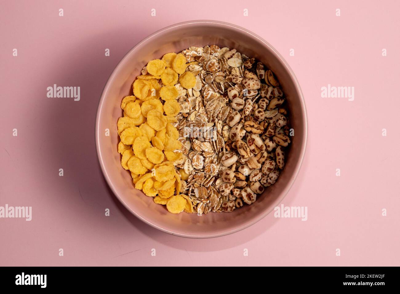 Verschiedene Frühstücksarten Müsli in einer rosa Schale. Maisflocken gerollter Hafer und gepuffter Weizen. Rosa Hintergrund. Stockfoto