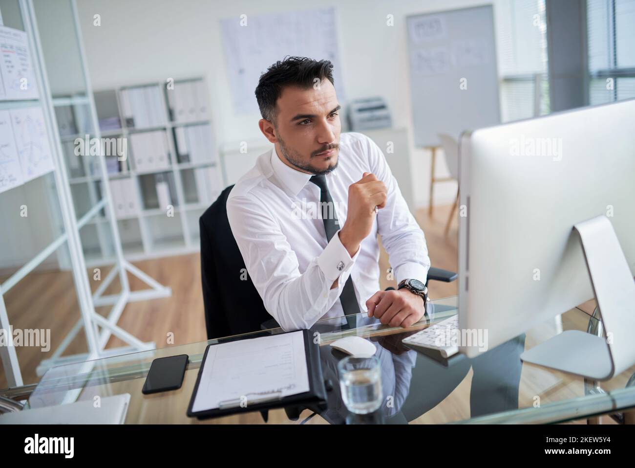 Selbstbewusster, gutaussehender Geschäftsmann, der an seinem Arbeitsplatz am Computer arbeitet Stockfoto