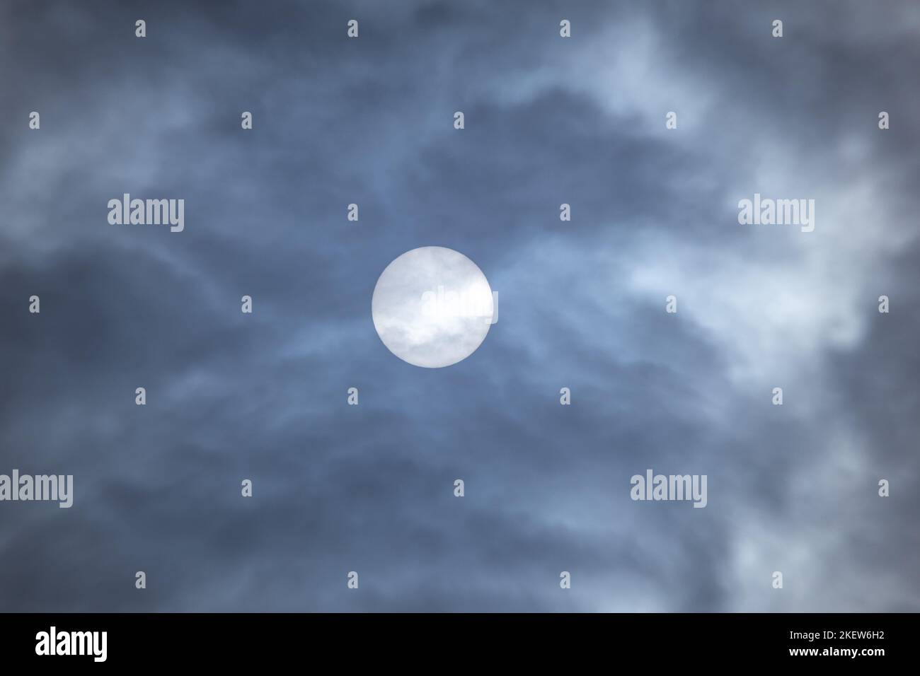 Großer Sonnenkreis, der tagsüber durch Wolken schaut. Sonne in dunkler Wolkenlandschaft Naturphänomen Hintergrund in grauen Farben Stockfoto