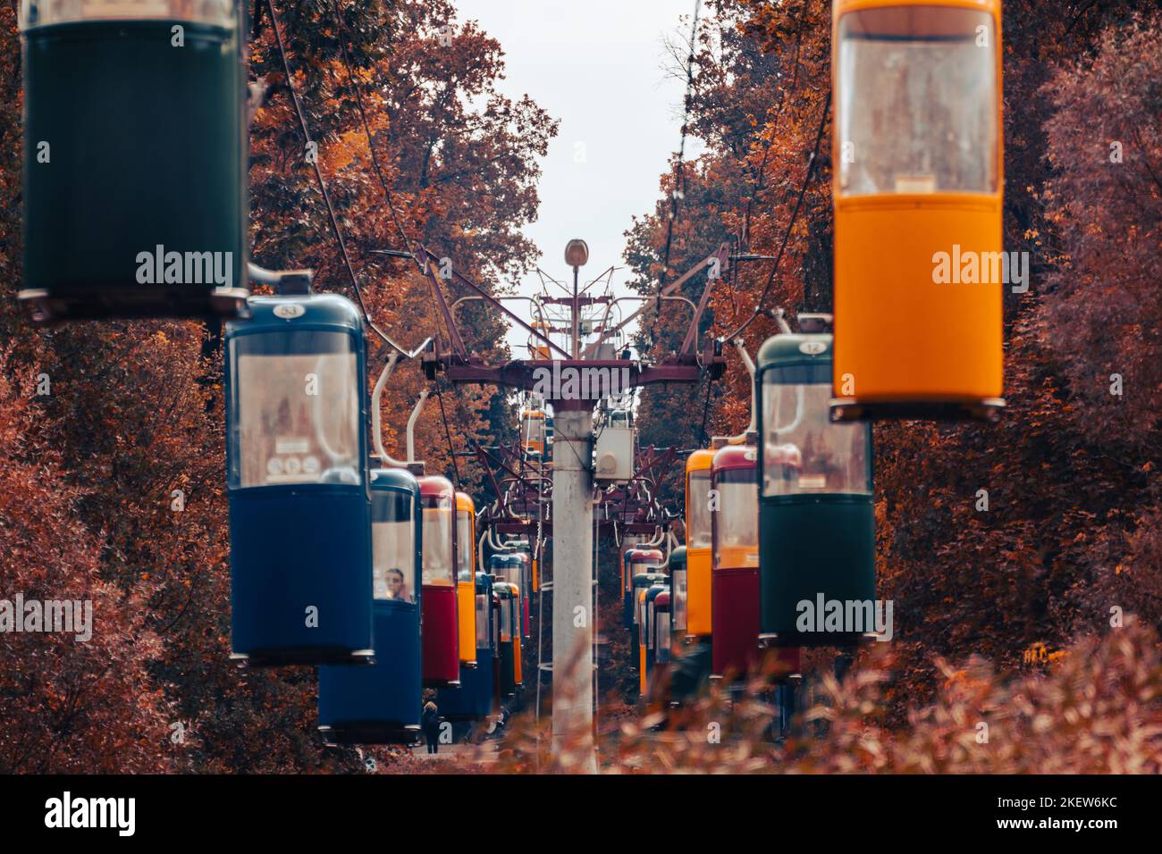 Bunte Seilbahnkabinen im Herbstwald mit goldenen Bäumen und grauem Himmel. Farblich abgestuft Stockfoto