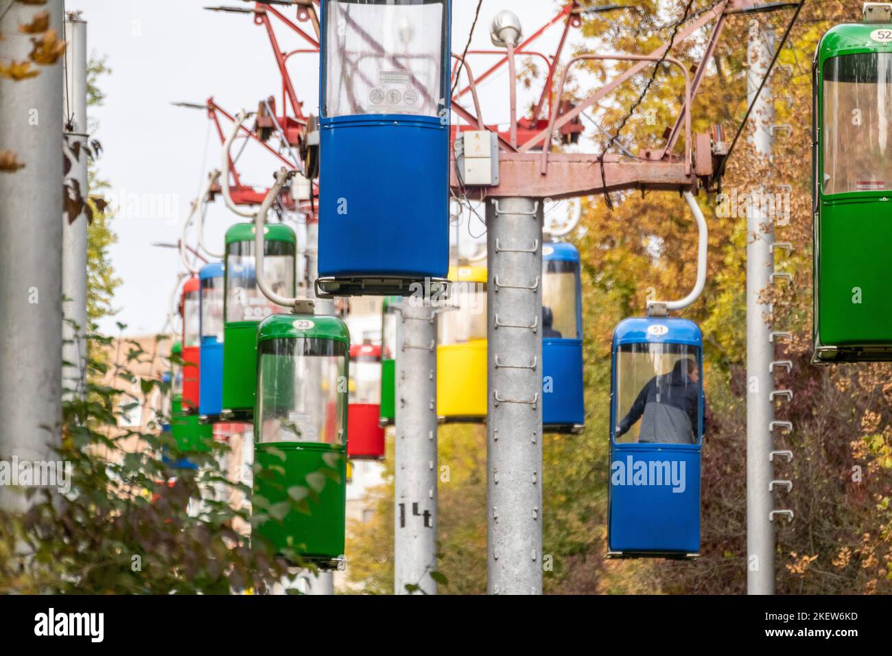 Farbenfrohe Kabinen für den Transport der Seilbahn im Herbst im Vergnügungspark der Stadt Charkiw mit goldenen Bäumen und grauem Himmel Stockfoto
