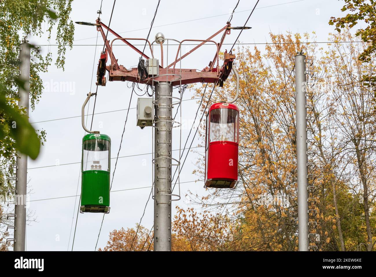 Farbige rote und grüne Seilbahnkabinen im goldenen Kharkiv-Stadtpark im Herbst. Standsäule mit Seilbahnkabinen Stockfoto