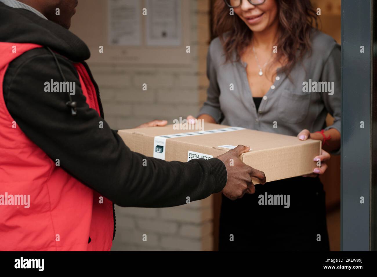Hände eines jungen afroamerikanischen Kuriers, der die verpackte Bestellung an eine Kundin des Zustelldienstes übergibt, während er vor ihr steht Stockfoto
