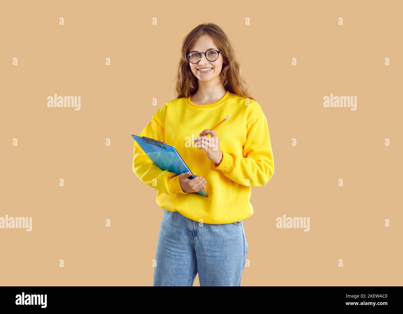 Happy Casual Teenager-Mädchen posiert auf hellbeigem Hintergrund mit Zwischenablage zum Aufschreiben von Ideen. Stockfoto