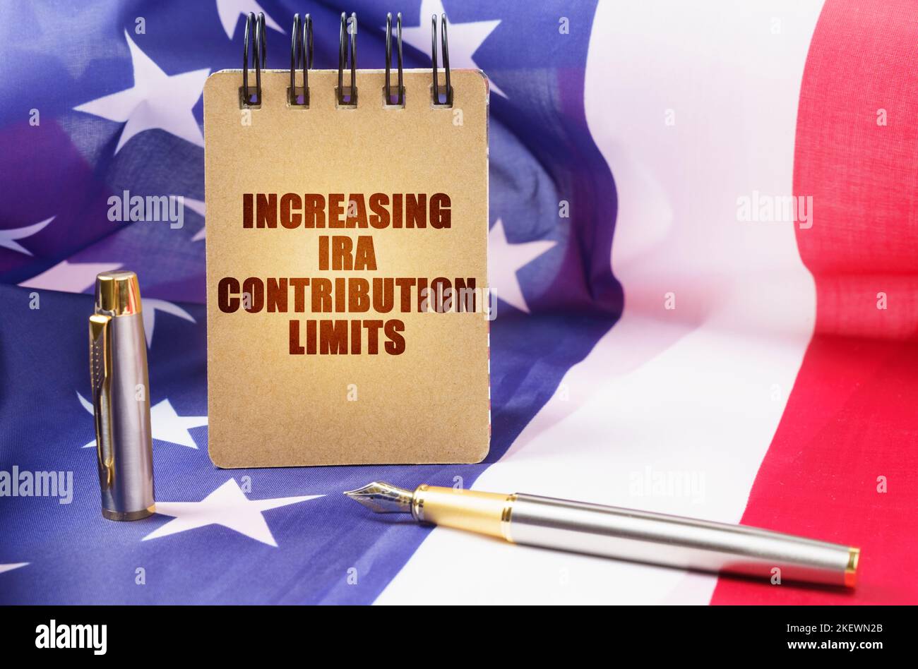 Geschäftskonzept. Vor dem Hintergrund der amerikanischen Flagge befindet sich ein Notizblock mit der Aufschrift - Erhöhung der IRA-Beitragslimits Stockfoto Geschäftskonzept. Vor dem Hintergrund der amerikanischen Flagge befindet sich ein Notizblock mit der Aufschrift - Erhöhung der IRA-Beitragslimits Stockfoto