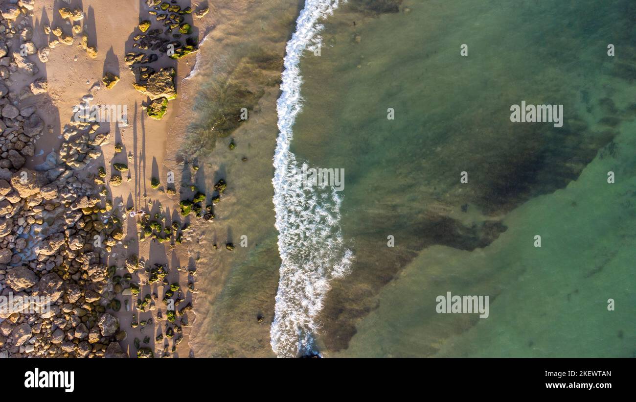 Atemberaubende szenische Drohne Luftaufnahme des Strandes und des Ozeans mit ruhigen Wellen während eines Sonnenuntergangs mit lebendigen Farben. Algarve, Portugal. Klares Wasser. Feiertage Stockfoto
