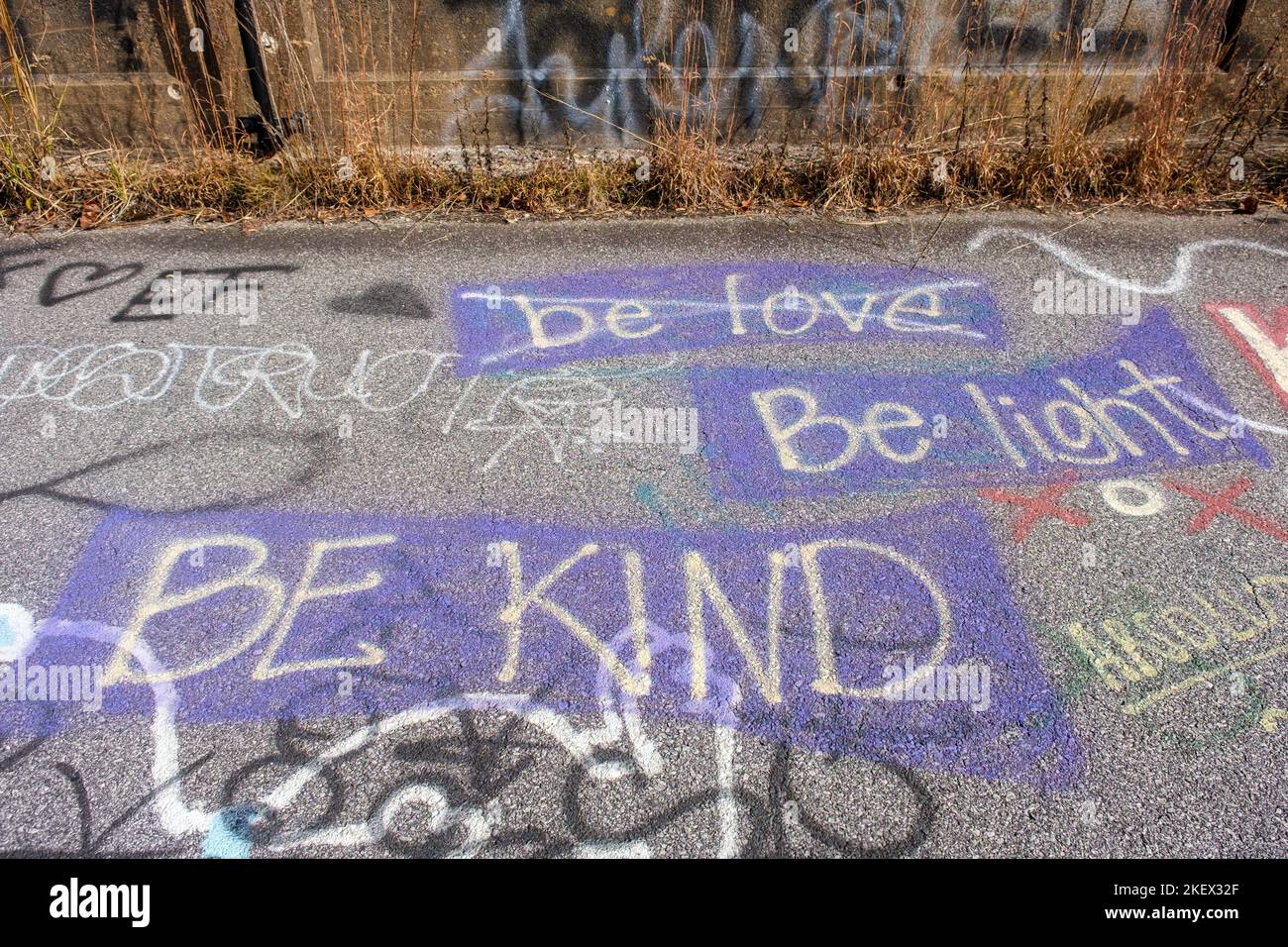 „Be Kind, Be Light, Be Love“-Graffiti in lila und weiß auf einer verlassenen Straße. Stockfoto