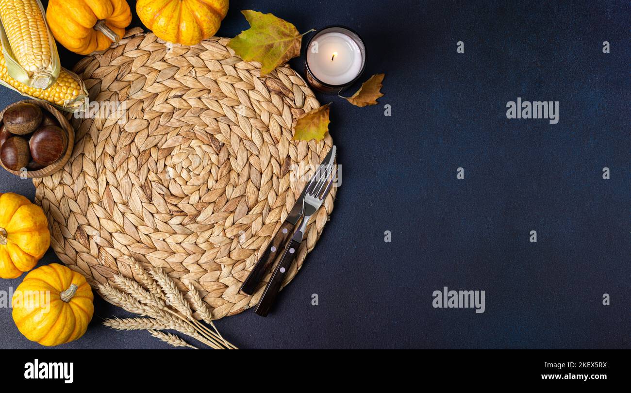 Gemütlicher Hygge-Tisch. Draufsicht auf Korbstrohunterlage, Kürbisse, Herbstblätter und Besteck auf grünem Tisch. Herbsttischeinstellung. Festliches Erntedankfest b Stockfoto