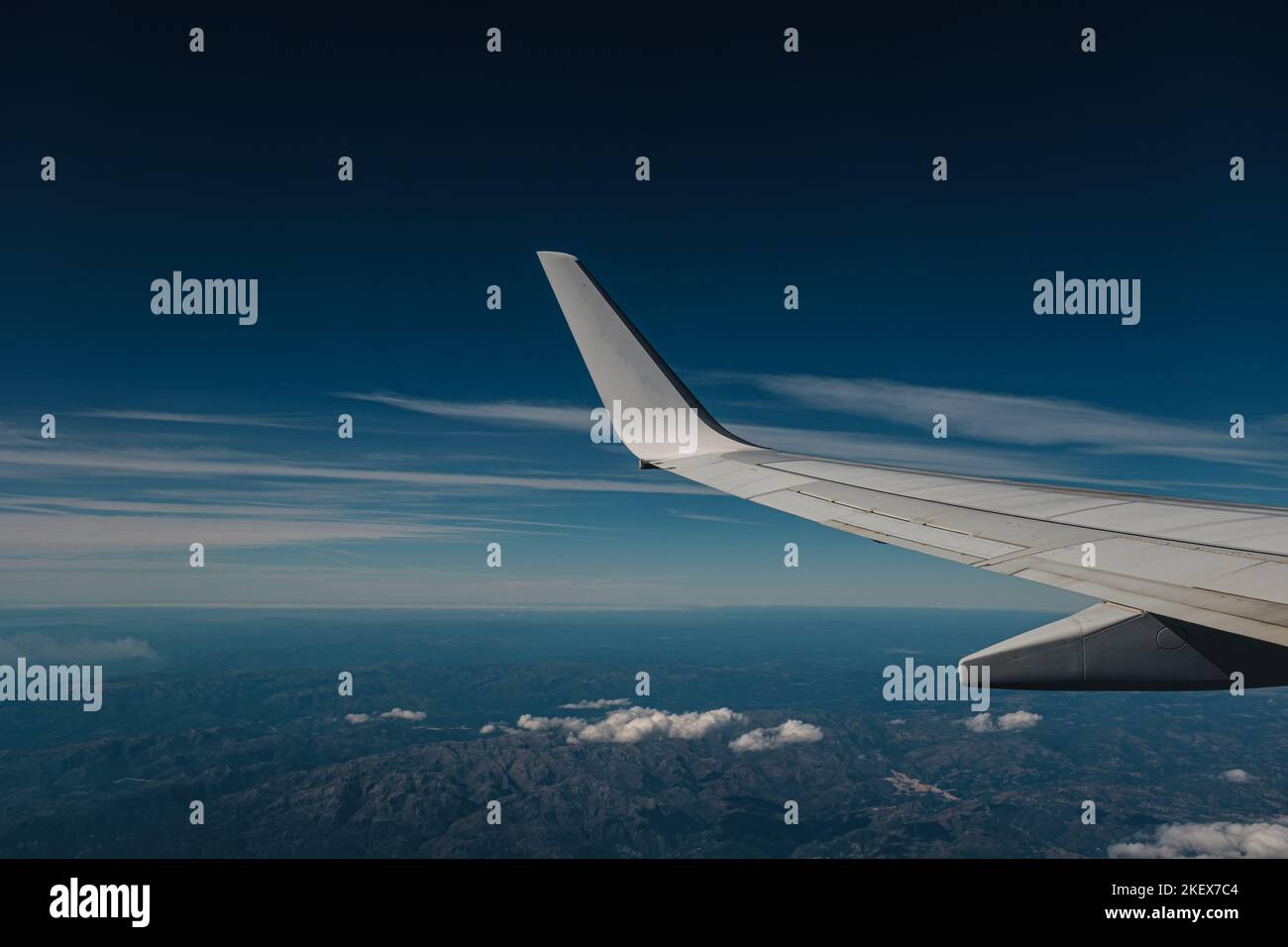 Landschaftlich schöner Blick auf die blaue Landschaft von einem Flugzeugflügel, der über die Berge und einige Wolken fliegt Stockfoto