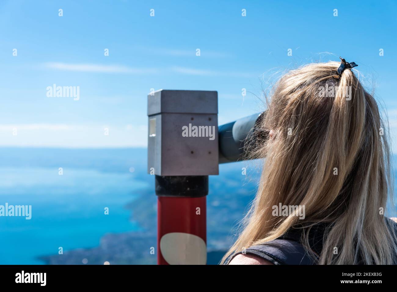 Reife blonde Frau, die durch ein Fernglas schaut und den Genfer See in der Schweiz überblickt. Stockfoto