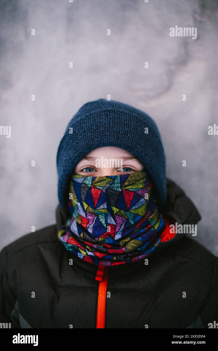 Boy mit blauen Augen liegt im Schnee mit Beanie, Halswärmer und Skimantel Stockfoto