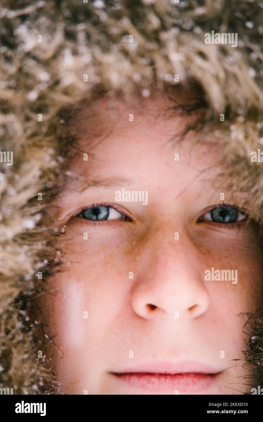 Nahaufnahme des Jungen Gesichts mit blauen Augen, Sommersprossen und Schneeflocken auf dem Fell Stockfoto