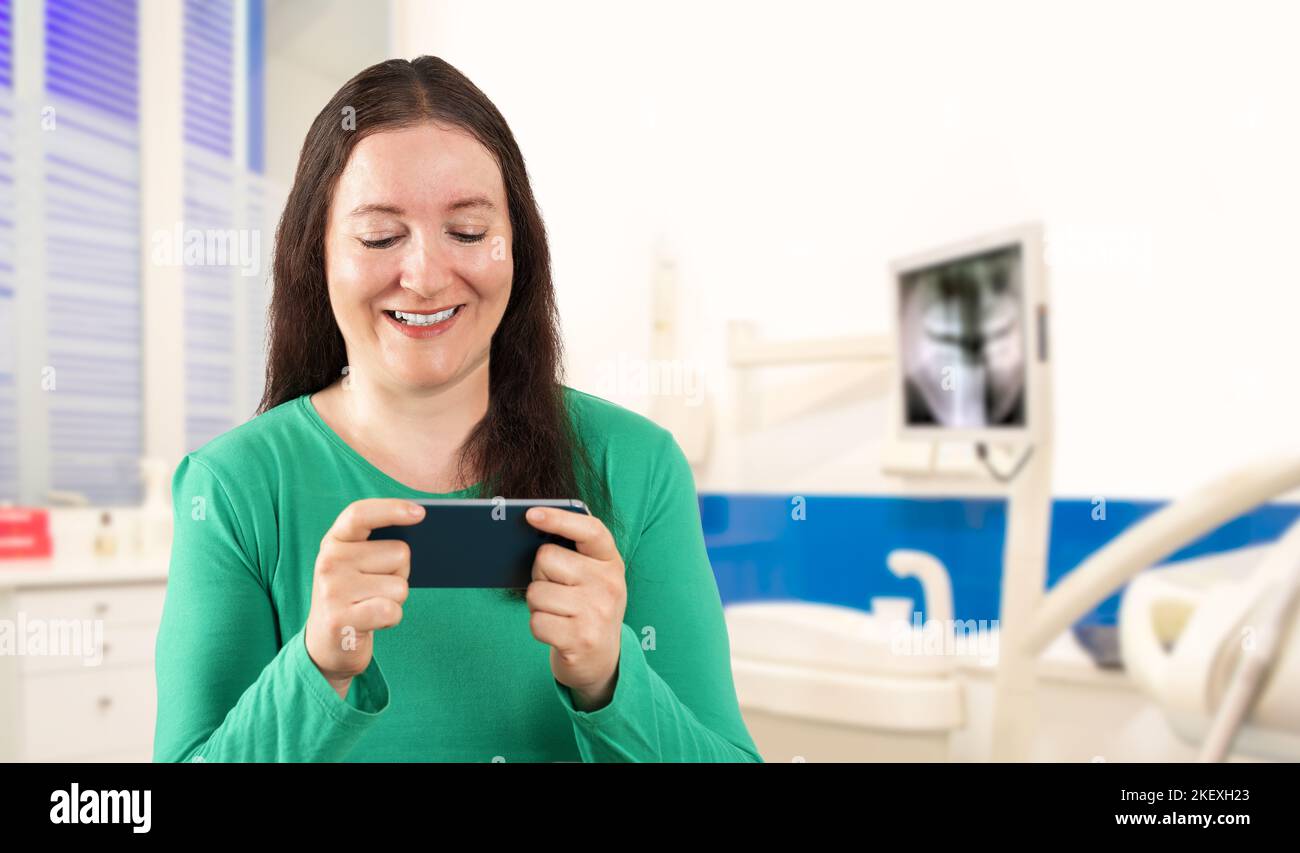 Hispanische Frau lächelt selbstbewusst mit dem Smartphone im Sprechzimmer Stockfoto