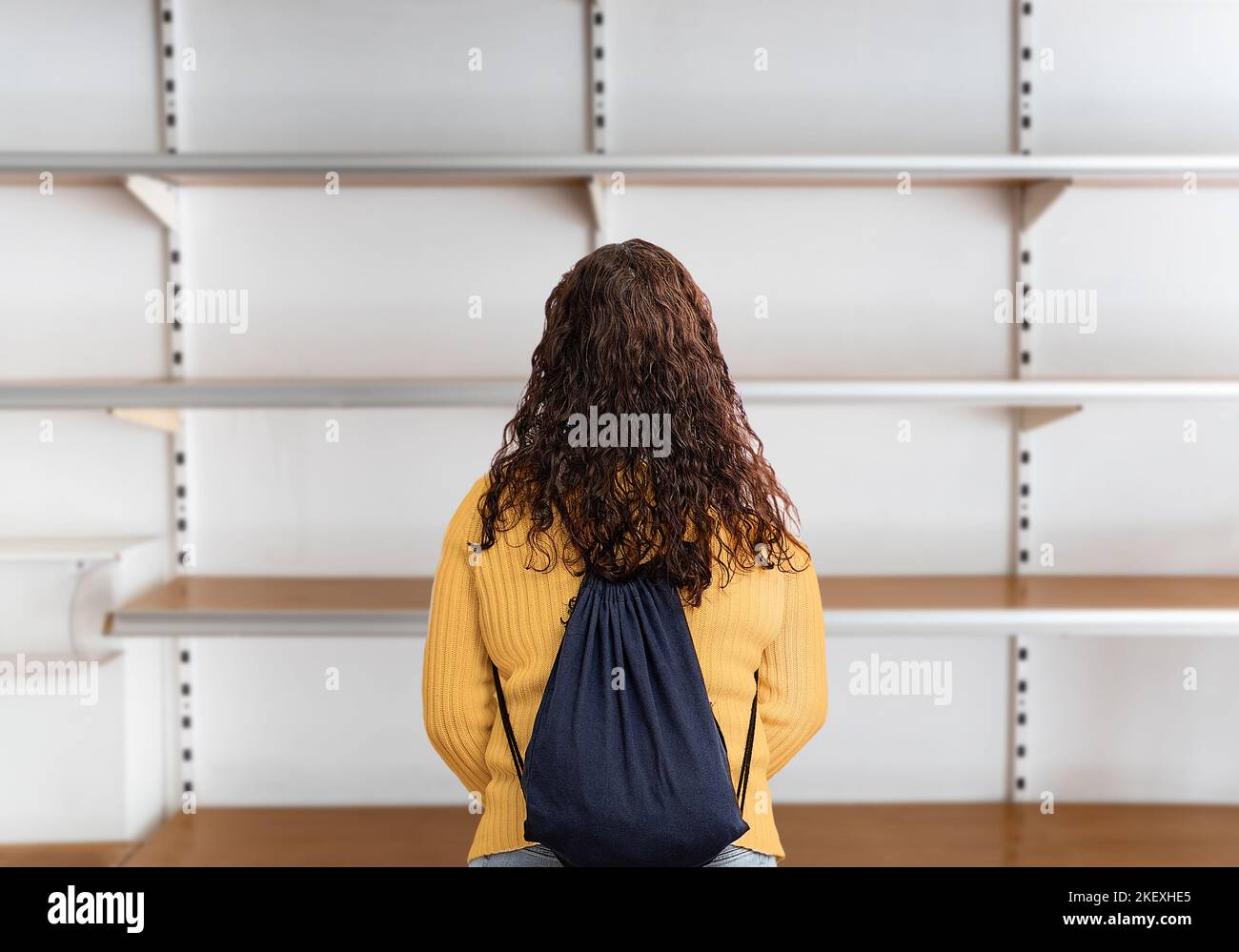 Rückansicht einer jungen Frau, die in einem Supermarkt vor einem leeren Regal steht Stockfoto