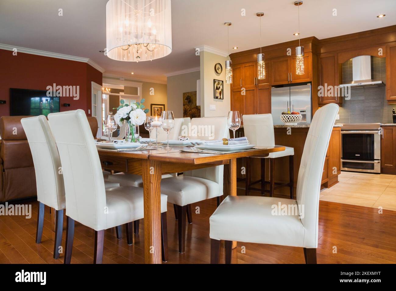 Dunkel gebeizter Eichenholztisch mit weißem Leder mit hoher Rückenlehne und Holzstühlen im Esszimmer-Küchenbereich in luxuriösem, zeitgenössischem Landhausstil. Stockfoto