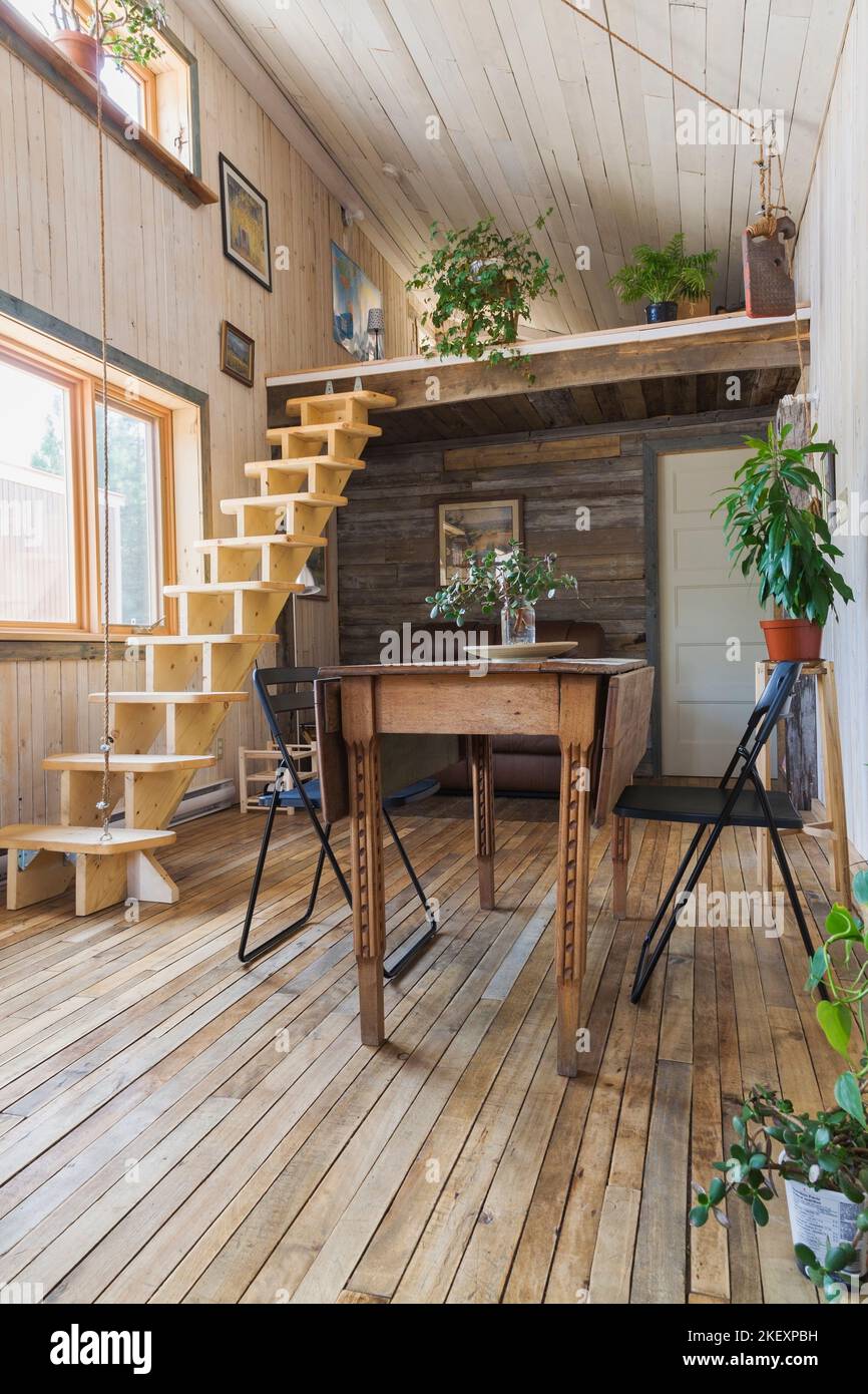 Esstisch aus Holz mit Klappstühlen und einziehbarer Kiefernholztreppe, die  zum Schlafzimmer und Wohnbereich im Zwischengeschoss mit braunem Ledersofa  führt Stockfotografie - Alamy