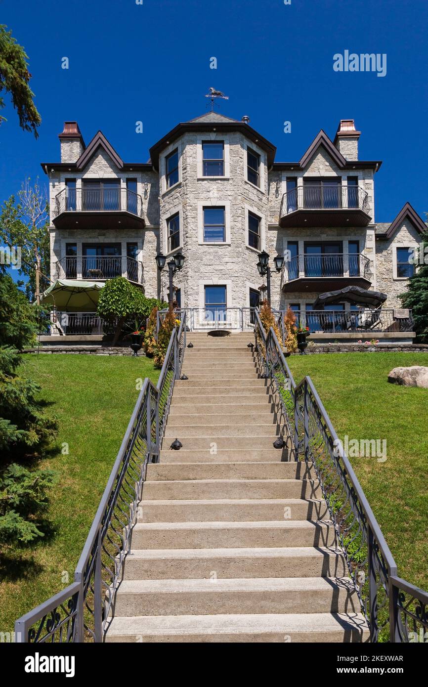 Betontreppen mit schwarzen schmiedeeisernen Geländern, die im Sommer auf die Rückseite eines luxuriösen grauen Steins mit braunen Zierleisten im Cottage-Stil führen. Stockfoto