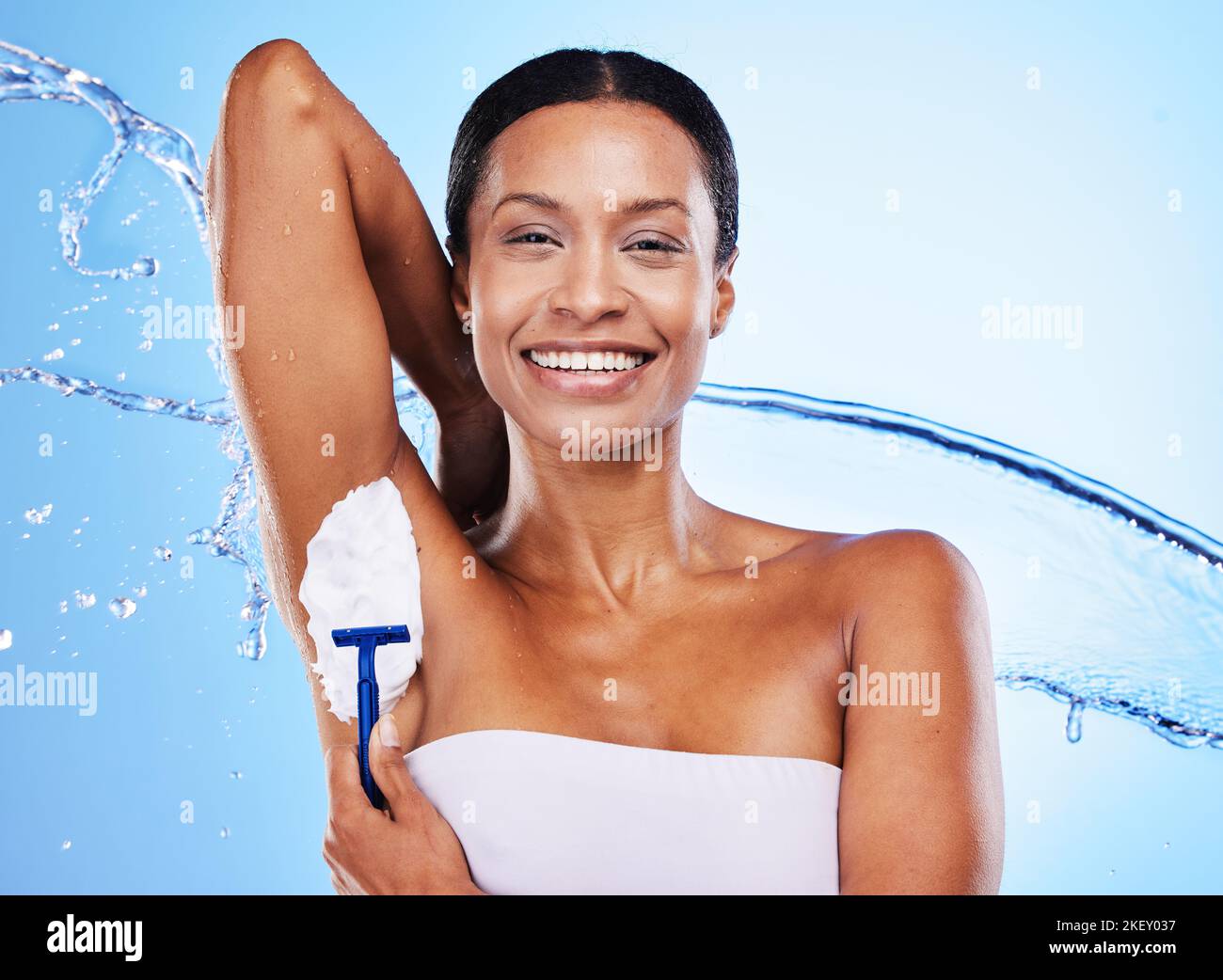 Schwarze Frau, Achselrasur mit Creme und Rasiermesser, Schönheit für die Pflege, Duschwasser spritzen mit blauem Studiohintergrund. Hygiene, Schaumprodukt und Stockfoto