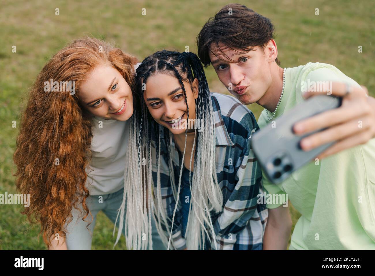 Drei junge, glücklich lächelnde kaukasische Teenager, die im Sommer Selfie im Park machen und verrückt werden und lachen. Sonnenuntergang Licht.Glückliche und positive Emotionen. Stockfoto