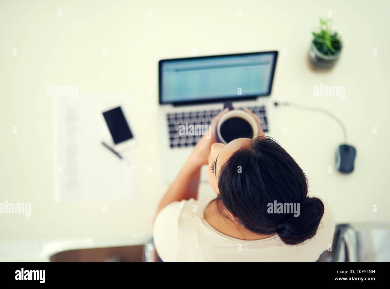 Zeit für eine kurze Kaffeepause. High-Angle-Aufnahme einer jungen Geschäftsfrau, die zu Hause an ihrem Laptop arbeitet. Stockfoto