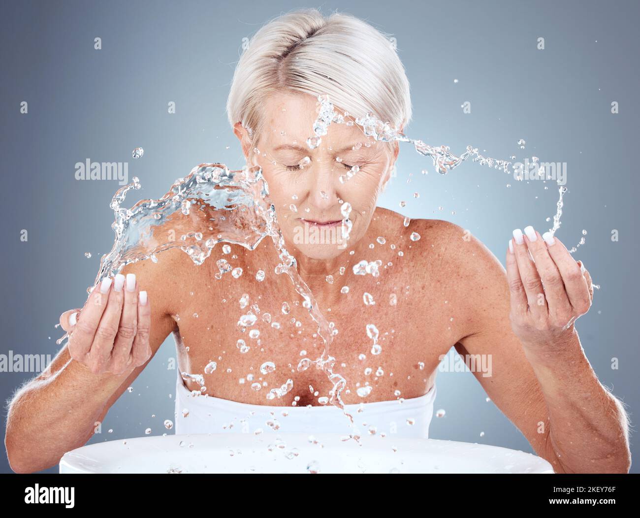Ältere Frau, Wasserspritzer und Hautpflege mit Reinigung, Wellness und Gesichtswäsche vor grauem Studiohintergrund. Ältere Modelle, Schönheits- und Gesichtsbehandlungen Stockfoto