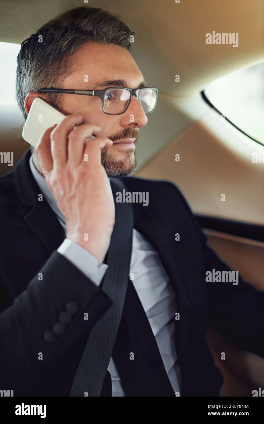 Heute alle meine Meetings abbrechen. Ein Geschäftsmann, der sein Handy benutzt, während er auf dem Rücksitz eines Autos sitzt. Stockfoto